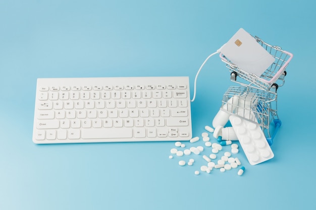 Shopping cart toy with medicaments and Keyboard. Pills, blister packs, medical bottles, thermometer, protective mask on a blue background. Top view with place for your text