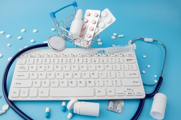 Shopping cart toy with medicaments and Keyboard. Pills, blister packs, medical bottles, thermometer, protective mask on a blue background.