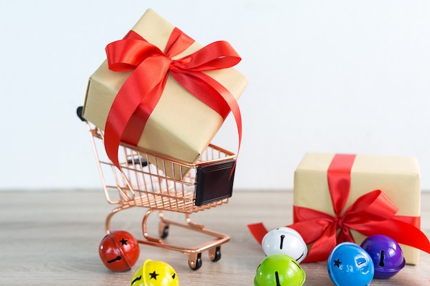 Shopping cart with Christmas gifts box Red ribbon and colorful bell on wood 