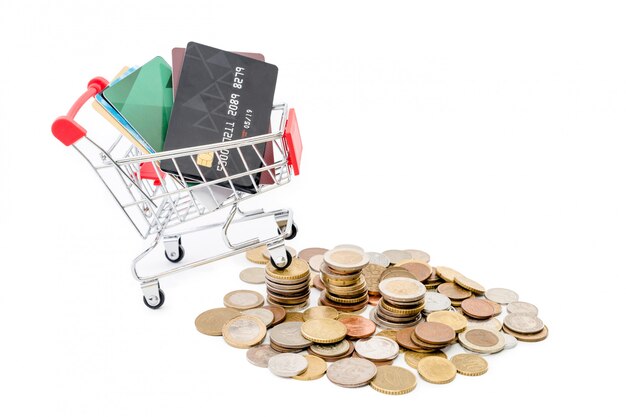 Shopping cart with credit cards is riding up a pile of coins on white background.