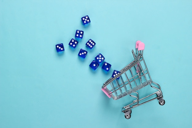 Shopping cart with dice on a blue pastel background. Good luck shopping. Top view