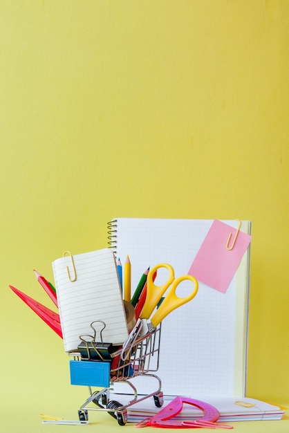 Shopping cart with different stationery on the yellow background