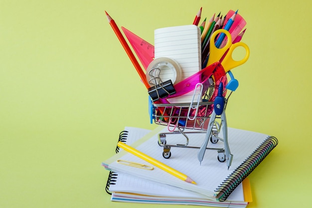 Shopping cart with different stationery on the yellow background