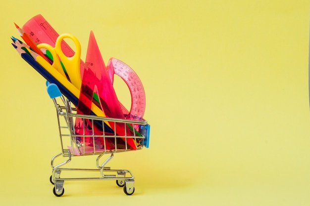 Shopping cart with different stationery on the yellow background.