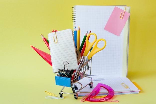 Shopping cart with different stationery on the yellow background.