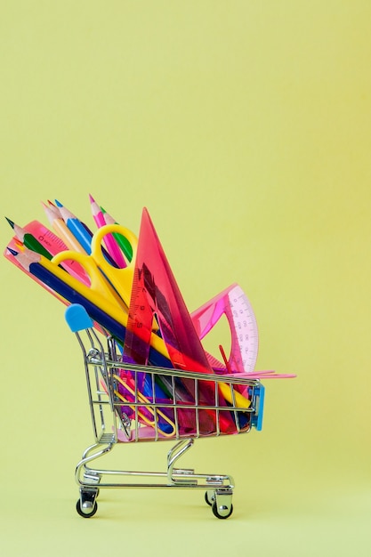 Photo shopping cart with different stationery on yellow