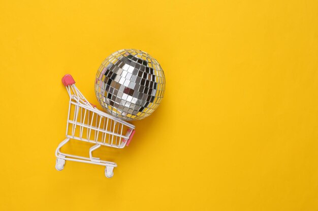 Shopping cart with disco ball on yellow background party concept creative minimal layout top view