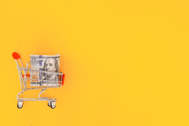 Shopping cart with dollar banknotes on a yellow backgroundBusiness finance shopping conceptSaving currency Investments Copy space