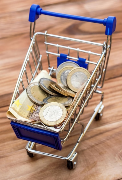 Shopping cart with euro bills and coins on the wooden table Financial concept