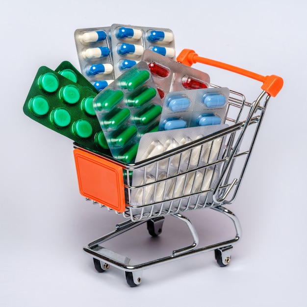 Shopping cart with full of medical pills or vitamins over light grey background