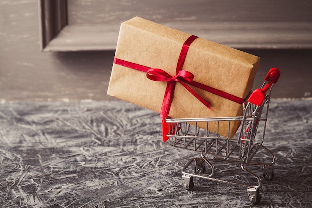 Shopping cart with gift or present on concrete table. 
