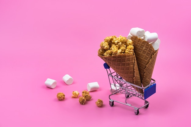 Shopping cart with ice cream cones on a pink background