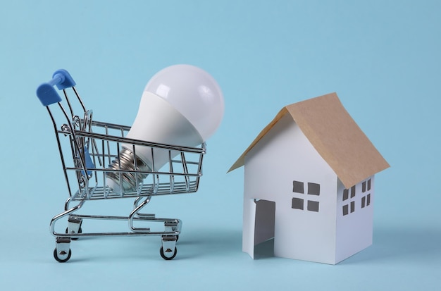 Foto carrello con lampadina a led e figurine di casa su sfondo blu economia dell'elettricità