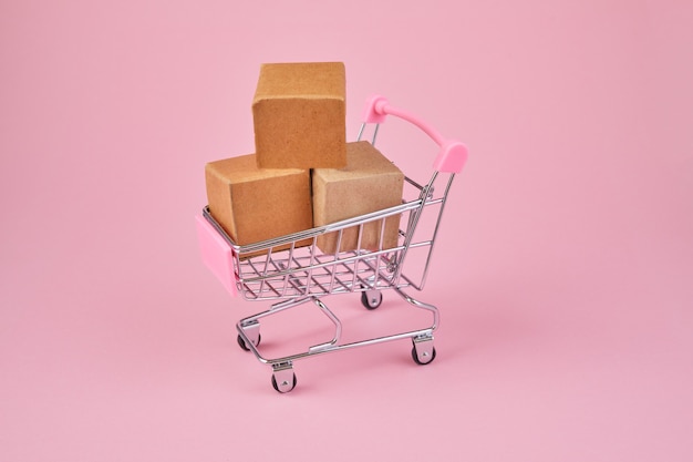 Photo shopping cart with package boxes on pink background. shop trolley full of parcels.