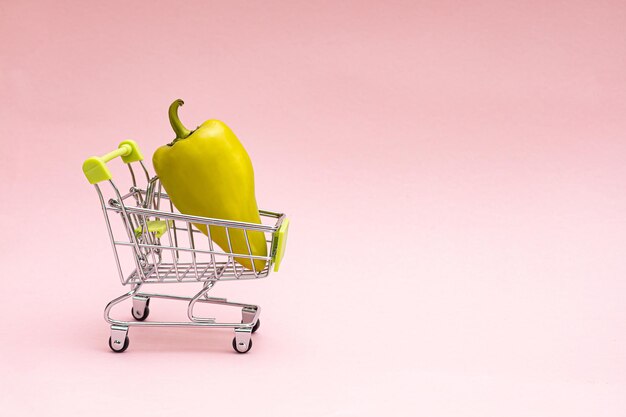 A shopping cart with peppers on a pink background Grocery and grocery store concept