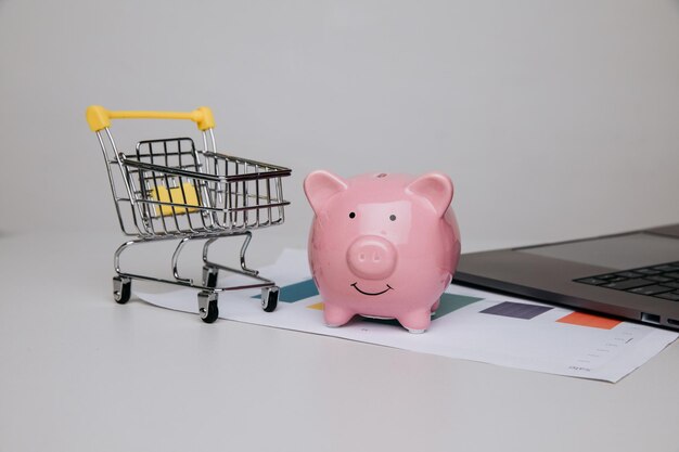 책상 위에 돼지 저금통과 노트북이 있는 쇼핑 카트 온라인 쇼핑 구매 및 비즈니스 개념