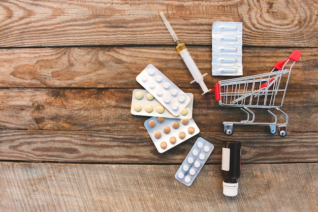 Shopping cart with pills, syringe on the old wood background.