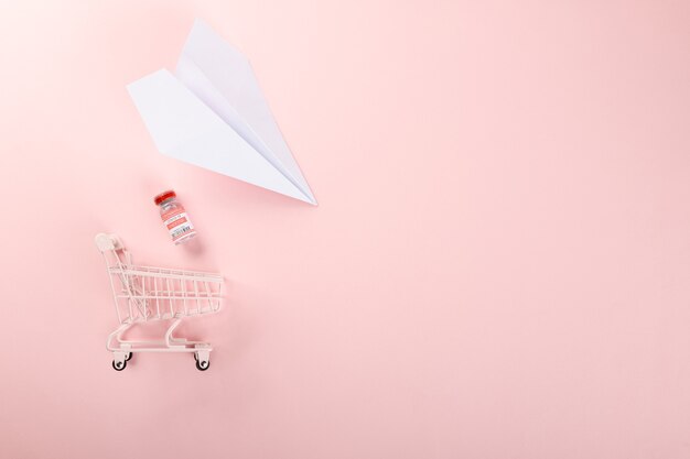 Shopping cart with vaccine vials bottles for vaccination against coronavirus and paper plane