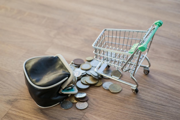 Shopping cart with wallet and coins on the wooden table