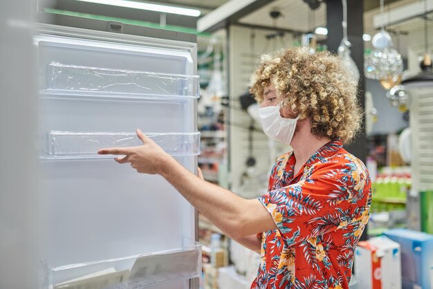 ショッピングのコンセプトスーパーマーケットで冷蔵庫を購入するフェイスマスクを持つ男