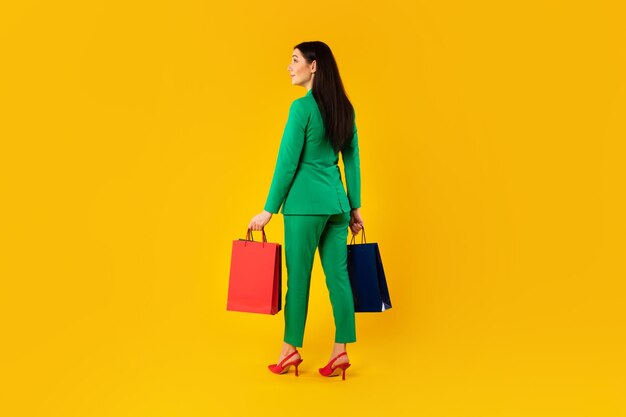 Shopping concept rear view of stylish lady holding shopper bags standing on yellow background free space