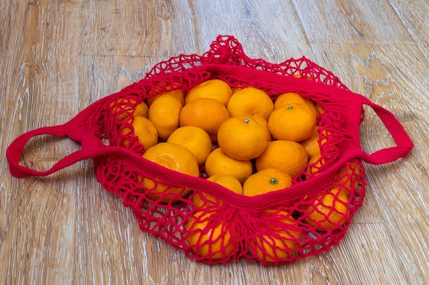 Shopping concept. Traditional fruit in Russia for New Year and Christmas. Tangerines lying in a red shopping bag on a wooden, top view, close-up. Healthy food concept