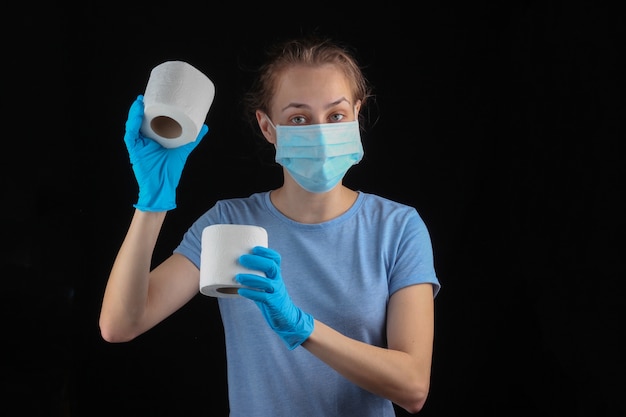 Shopping durante la pandemia 19-covid. la donna in mascherina e guanti medici tiene la carta igienica sulla parete nera.