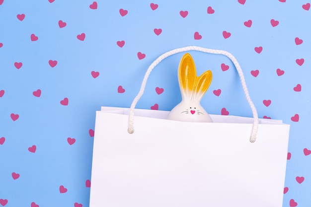 Shopping for Easter White paper shopping bag with white bunny on blue background with red hearts
