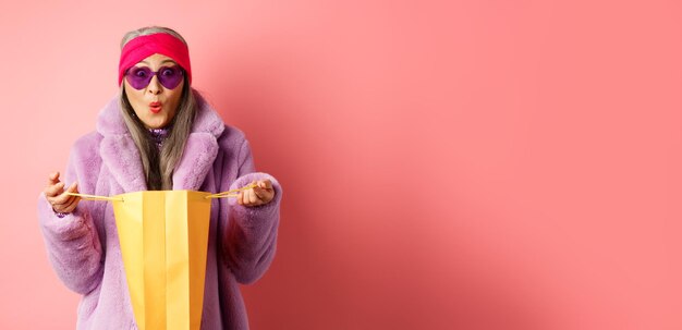 Photo shopping and fashion concept stylish asian elderly woman in sunglasses and faux fur coat open paper