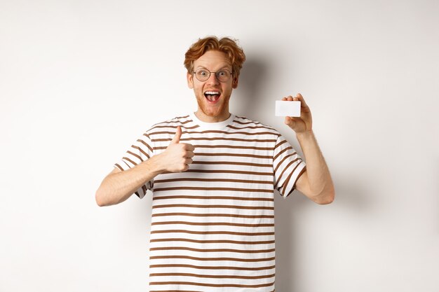 Photo shopping and finance concept. satisfied male bank client showing thumbs-up and plastic credit card, smiling happy at camera.