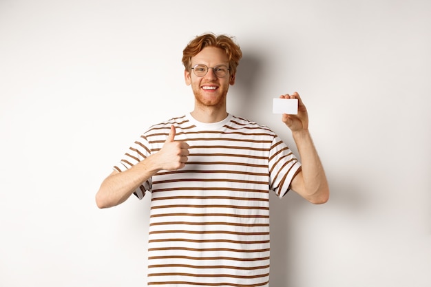 Shopping and finance concept. Satisfied male bank client showing thumbs-up and plastic credit card, smiling happy at camera.