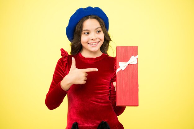 Shopping to find the perfect gift. Cute kid enjoying shopping. Little girl after shopping for gift. Small child holding gift box on yellow background. Shopping is fun. Smiling schoolgirl index finger.