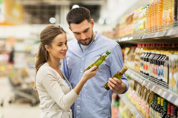 shopping, food, sale, consumerism and people concept - happy couple buying olive oil at grocery store or supermarket