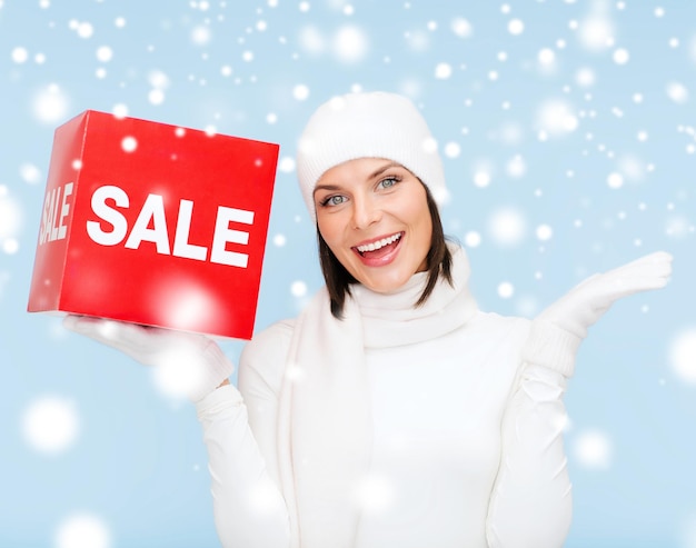 Фото Покупки, подарки, рождество, рождественская концепция - улыбающаяся женщина в зимней одежде с красным знаком продажи