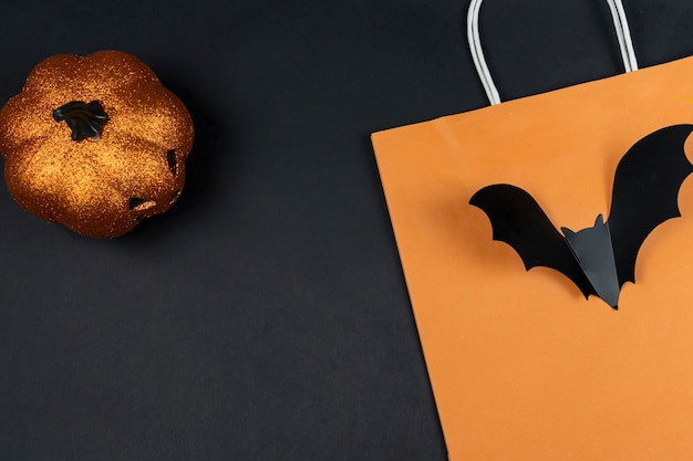 Shopping Halloween flat lay. Layout with copy space. Pumpkin about lantern, orange shopping bag and bat on a black background.