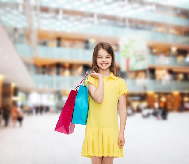 ショッピング、幸福と人々の概念-買い物袋と黄色のドレスで笑顔の少女