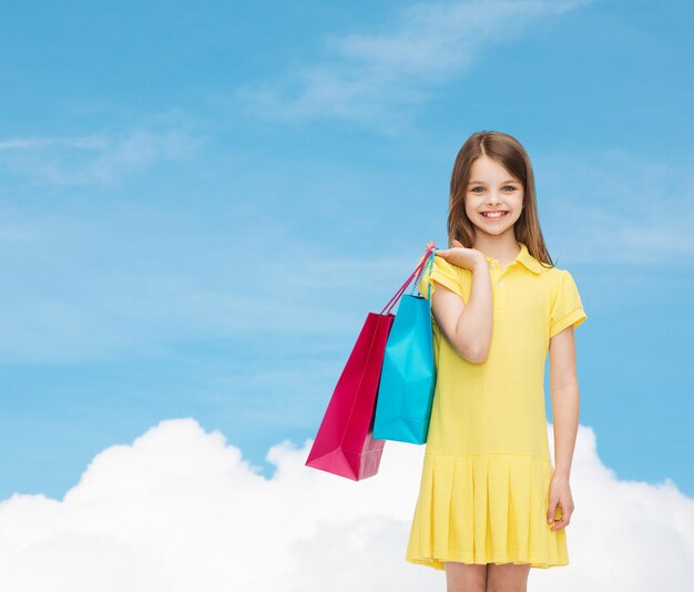 shopping, happiness and people concept - smiling little girl in yellow dress with shopping bags