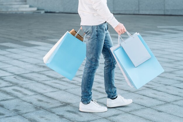 Uomo di acquisto consumismo urbano casuale gambe in jeans sacchetti di carta nelle mani