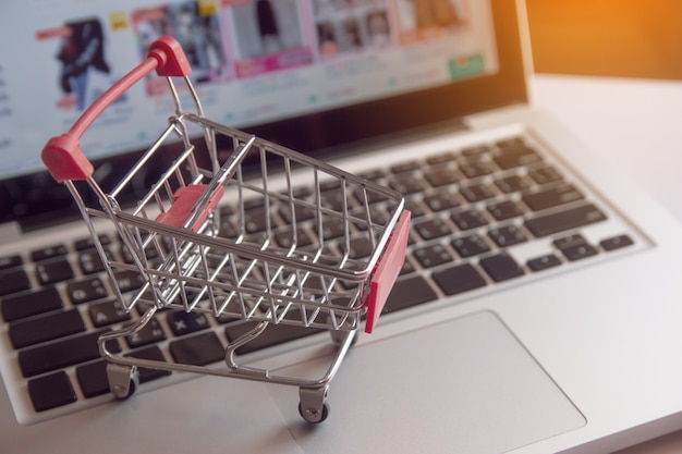 オンラインショッピングの概念 - ショッピングカートまたはラップトップのキーボード上のトロリー。オンラインWebでのショッピングサービス。コピースペースあり