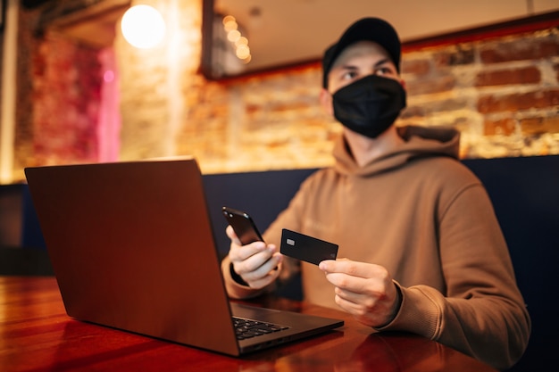 Shopping and online payment using cellphone, laptop and credit card. Man wearing mask during pandemic