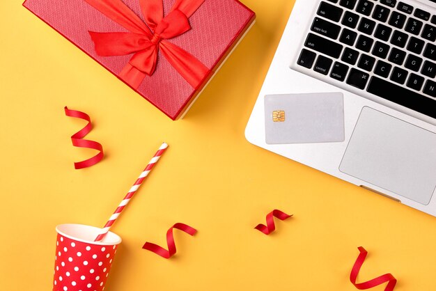 크리스마스 휴가를 위해 신용 카드로 온라인 쇼핑. 노란색 배경에 테이블에 선물이 있는 노트북