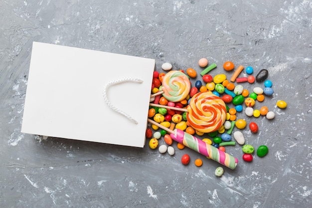 shopping paper gift bag in corner full of assorted traditional candies falling out on colored background with copy space Happy Holidays sale concept