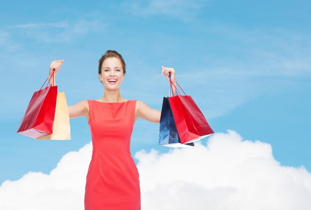 shopping, sale, christmas and holiday concept - laughing elegant woman in red dress with shopping bags