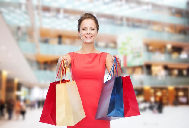 shopping, sale, christmas and holiday concept - smiling elegant woman in red dress with shopping bags