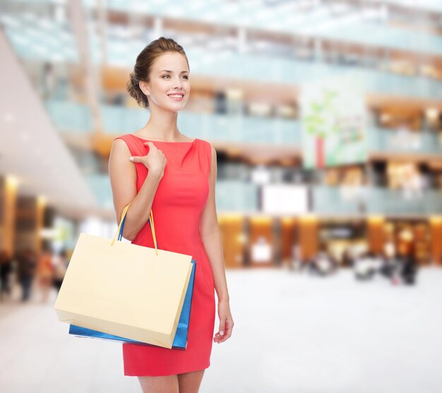 shopping, sale, christmas and holiday concept - smiling elegant woman in red dress with shopping bags