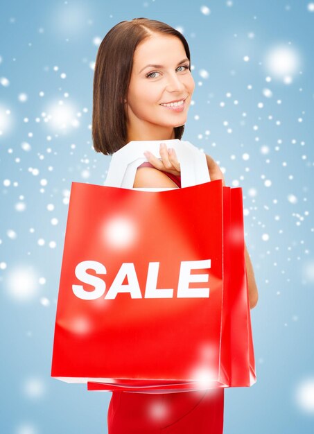 shopping, sale, gifts, christmas, x-mas concept - smiling woman in red dress with shopping bags