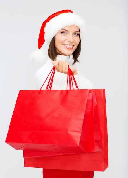 shopping, sale, gifts, christmas, x-mas concept - smiling woman in santa helper hat with shopping bags