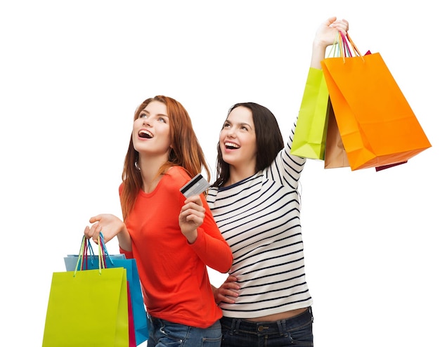 shopping, sale and gifts concept - two smiling teenage girls with shopping bags and credit card