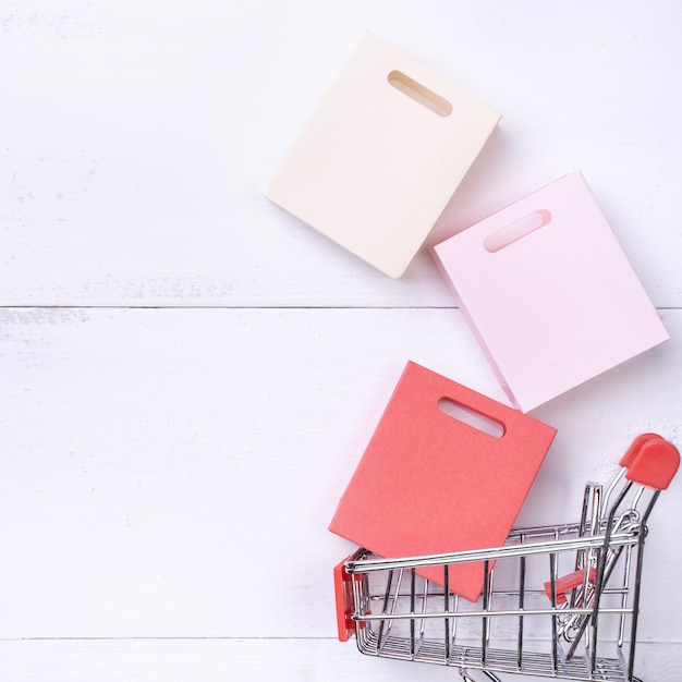 концепция сезона покупок, мини-тележка с красочным бумажным пакетом на белом деревянном столе, вид сверху, плоская планировка