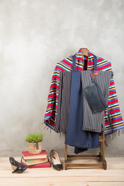 Shopping and style concept clothes rack with trendy striped pants and plaid shoes bag on wooden floor and grey concrete background